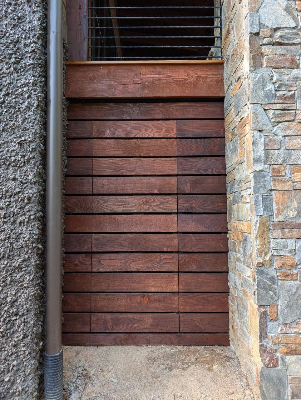The same panel closed — stained wood boards running flush and level with the skirting around it, no hardware or seam visible on the face.