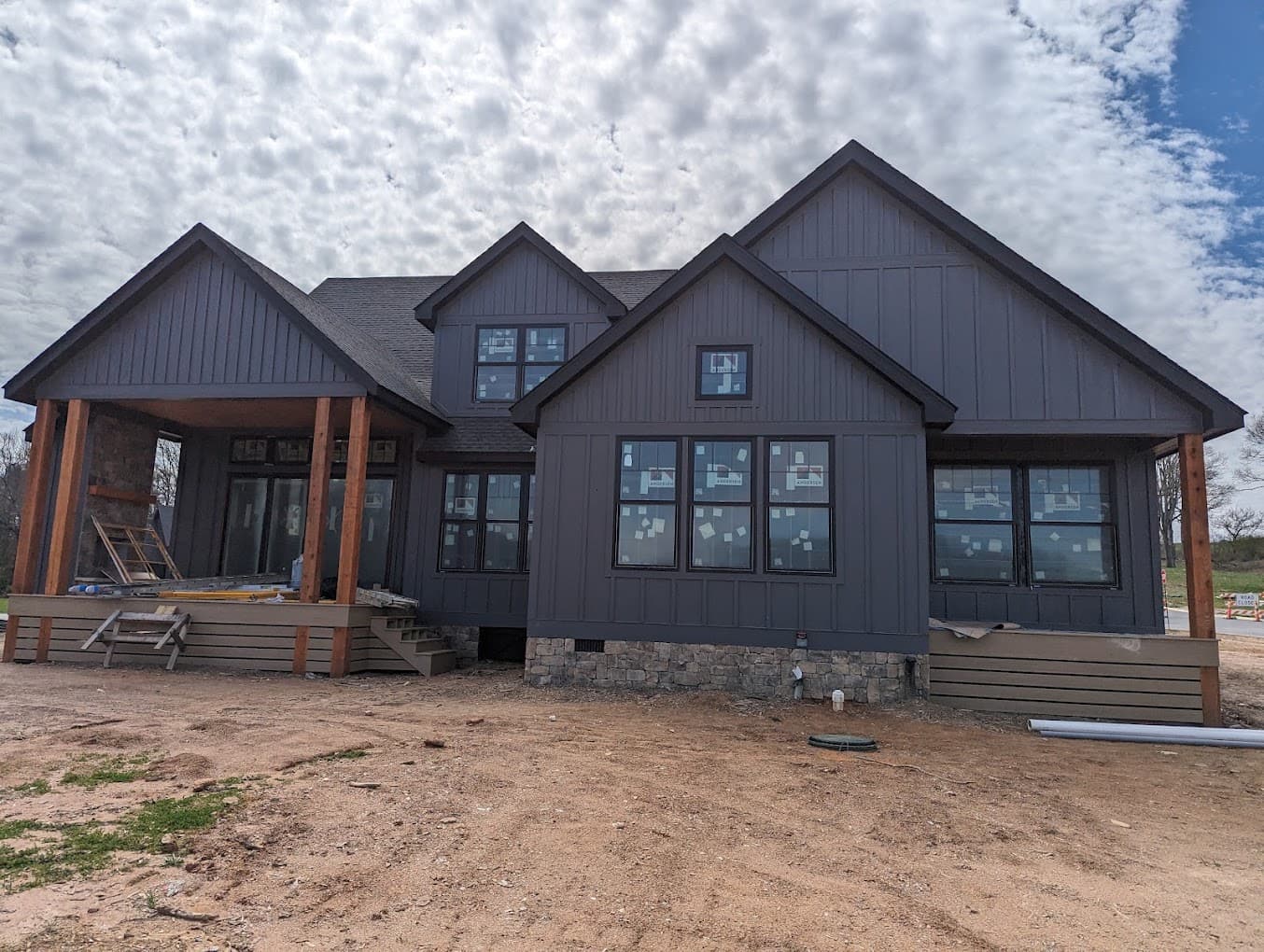 Finished dark board-and-batten siding on a custom home, with a cedar-post covered porch and stone skirt